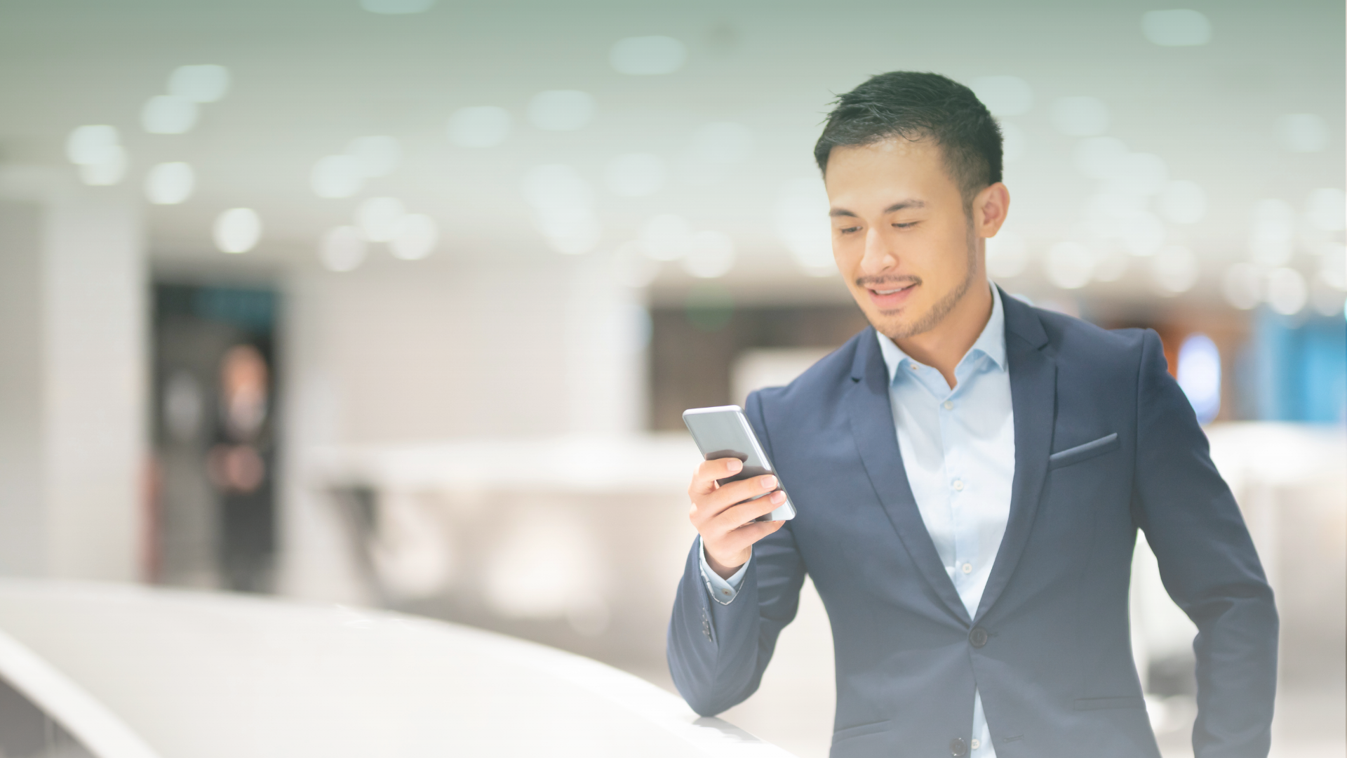 Malaysian entrepreneur in a business suit using a smartphone in a modern coworking space, embodying effective work prioritisation for the New Year 2024